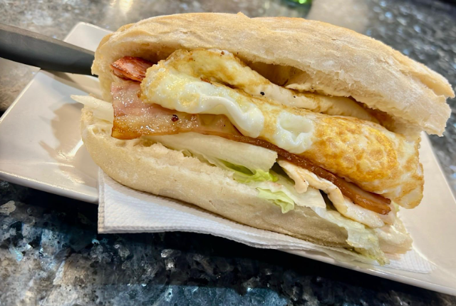 Un sándwich con huevos, tocino, lechuga y queso en un plato blanco.