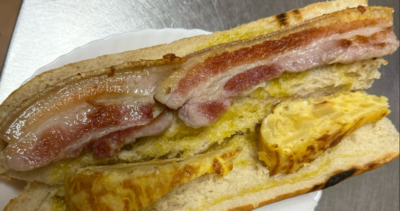 Un primer plano de un sándwich con tocino y huevos en un plato.