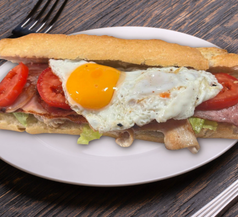 Un sándwich con huevos, tomates y tocino en un plato blanco.