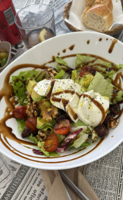 Una ensalada con tomates, aguacate y queso en un plato blanco.