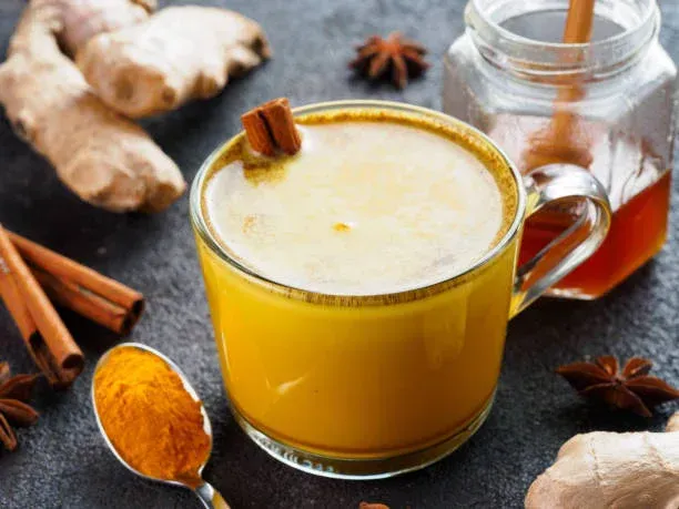 Latte de cúrcuma dorada en una taza de vidrio, con especias y miel cerca.