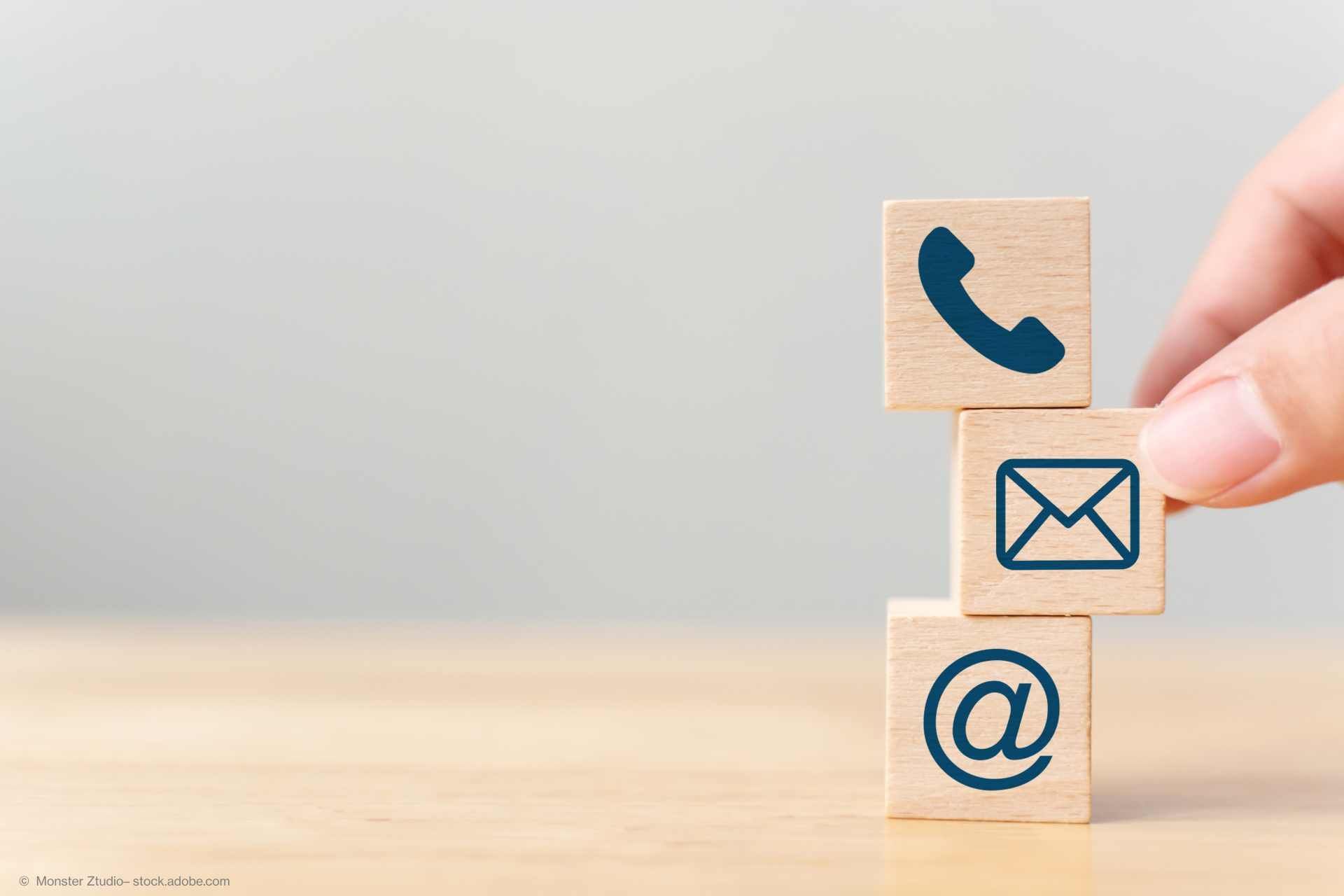 Eine Hand stapelt Würfel mit Kontaktsymbolen wie Telefon und E-Mail aufeinander