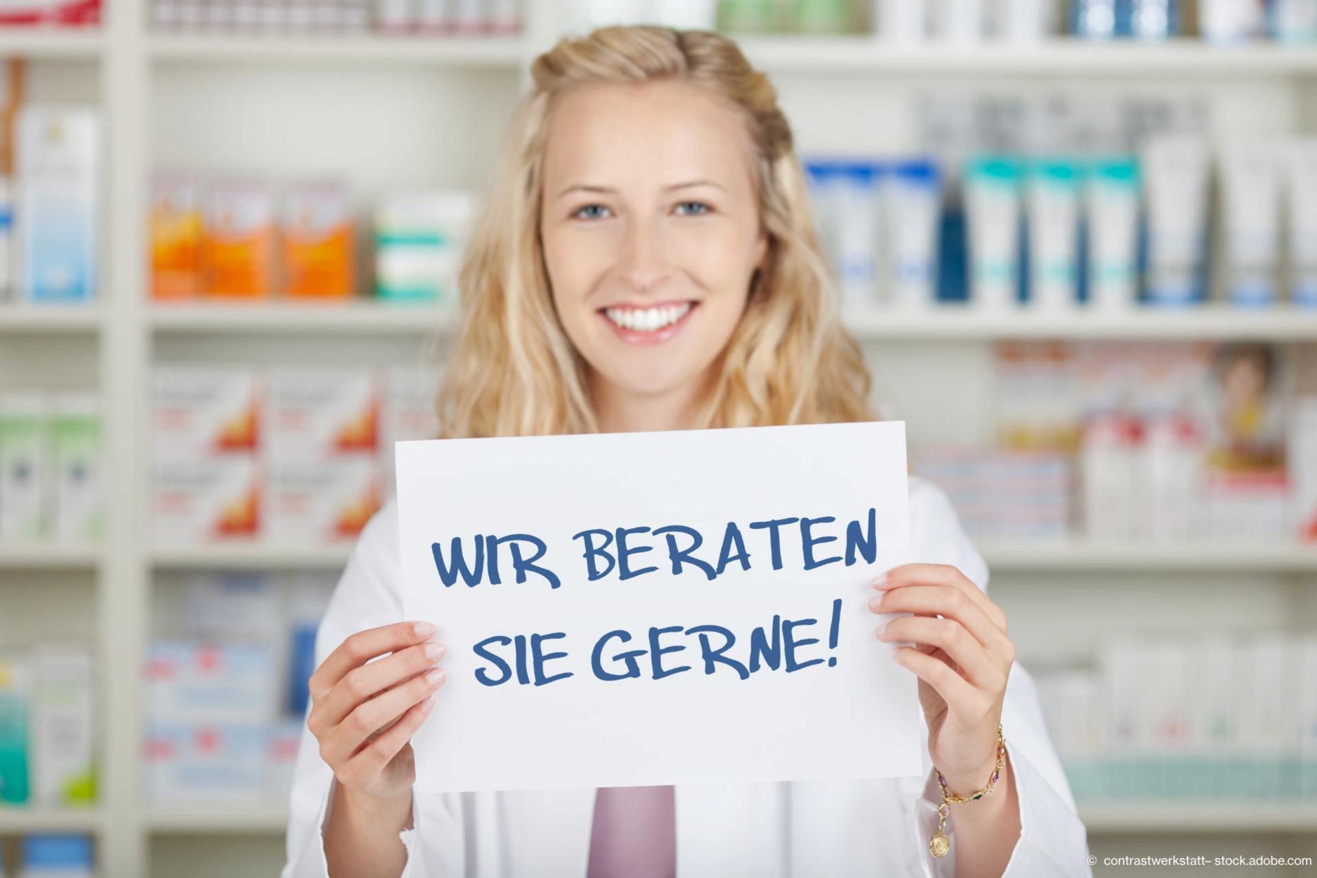 Eine Apothekerin mit strahlendem Lächeln zeigt ein Schild mit der Aufschrift