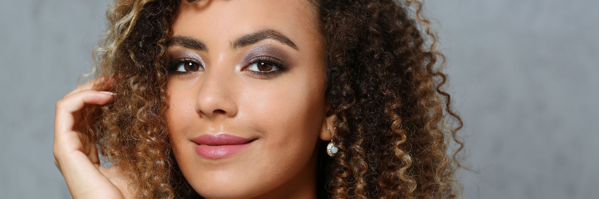 Femme aux cheveux bruns bouclés et au maquillage charbonneux, regardant l'objectif.