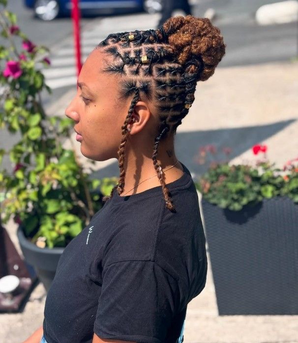 Femme avec des tresses géométriques et un chignon, quelques tresses pendantes, en extérieur.