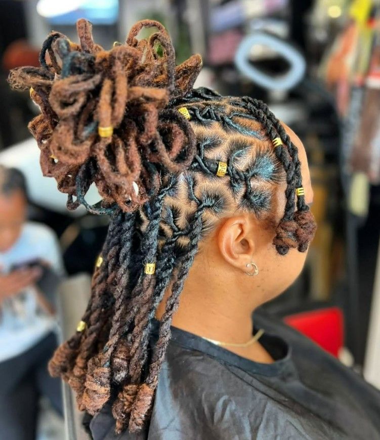 Femme aux dreadlocks brunes et noires coiffées avec des perles dorées, dans un salon de coiffure.