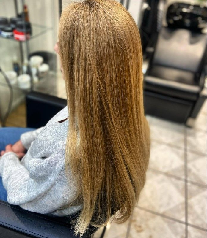 Une femme aux longs cheveux blonds dorés et raides est assise sur un fauteuil de salon.