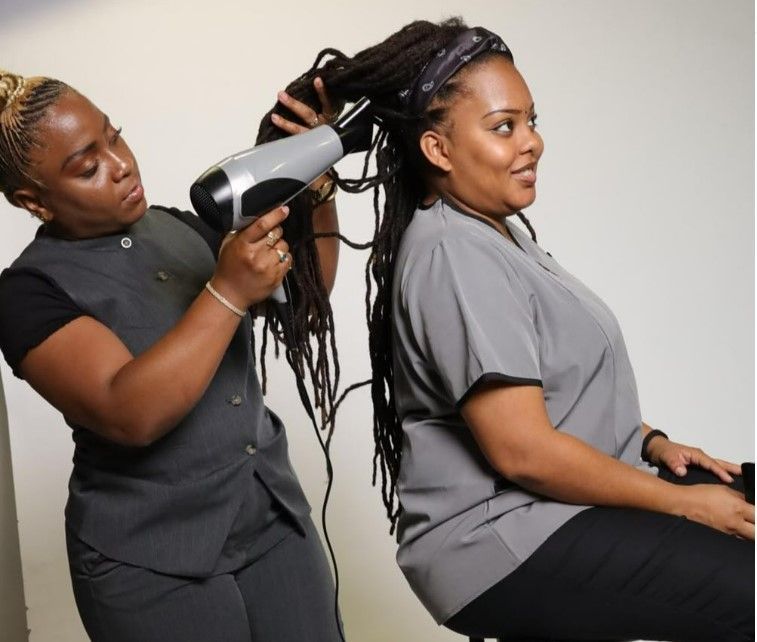 Une personne sèche les longues dreadlocks d'une femme dans un salon de coiffure.
