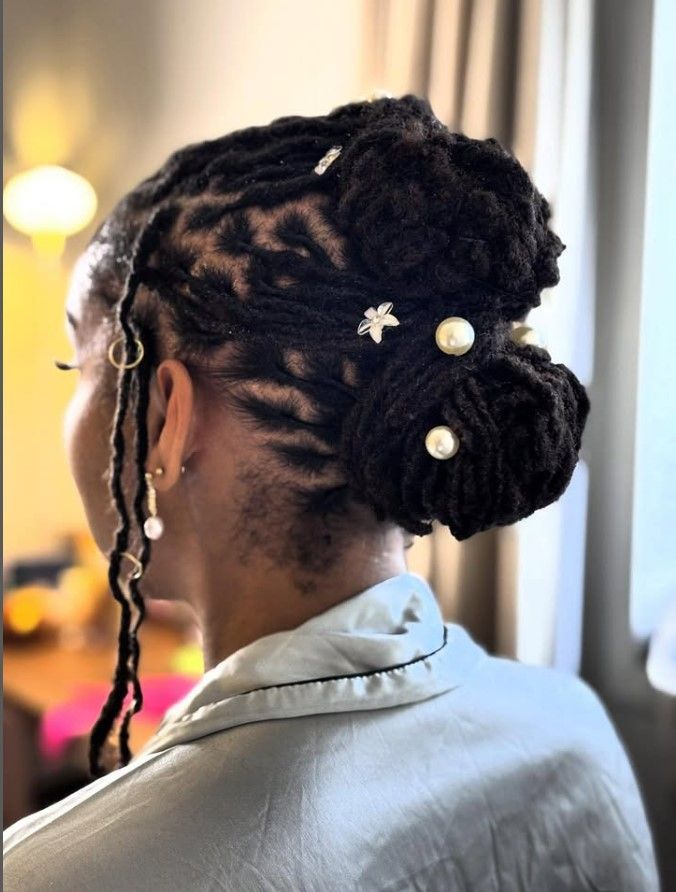 Personne aux cheveux foncés, dreadlocks coiffées en chignon, orné d'épingles à perles, portant un haut bleu clair.