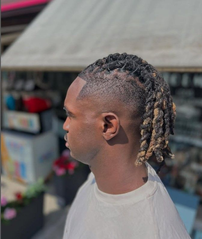 Un homme aux dreadlocks torsadées aux pointes blondes, à l'extérieur.