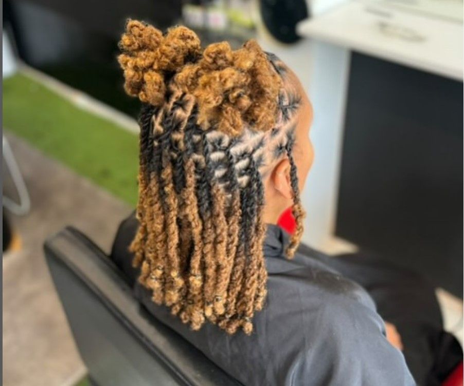 Femme avec des dreadlocks blondes et noires assises sur un fauteuil de salon, deux chignons sur le dessus.