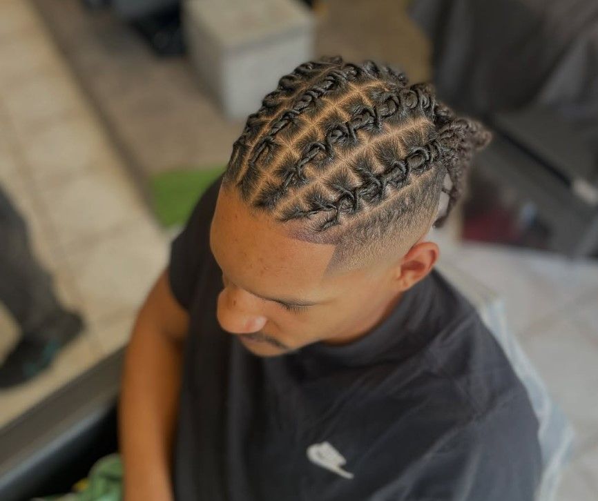 Homme avec une coiffure tressée soignée, à motif quadrillé, et une coupe dégradée à blanc.