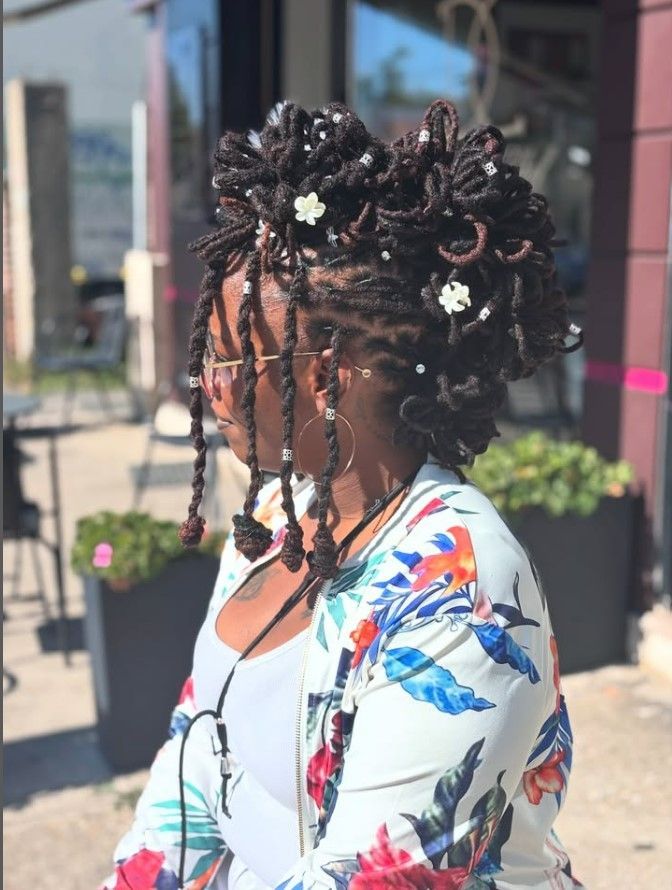 Femme aux cheveux tressés et coiffés en chignon, orné de petites fleurs blanches.