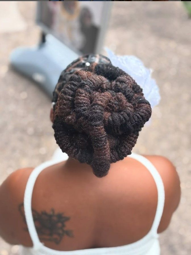 Femme en robe blanche, dos à la caméra, cheveux tressés en chignon avec un accessoire blanc.