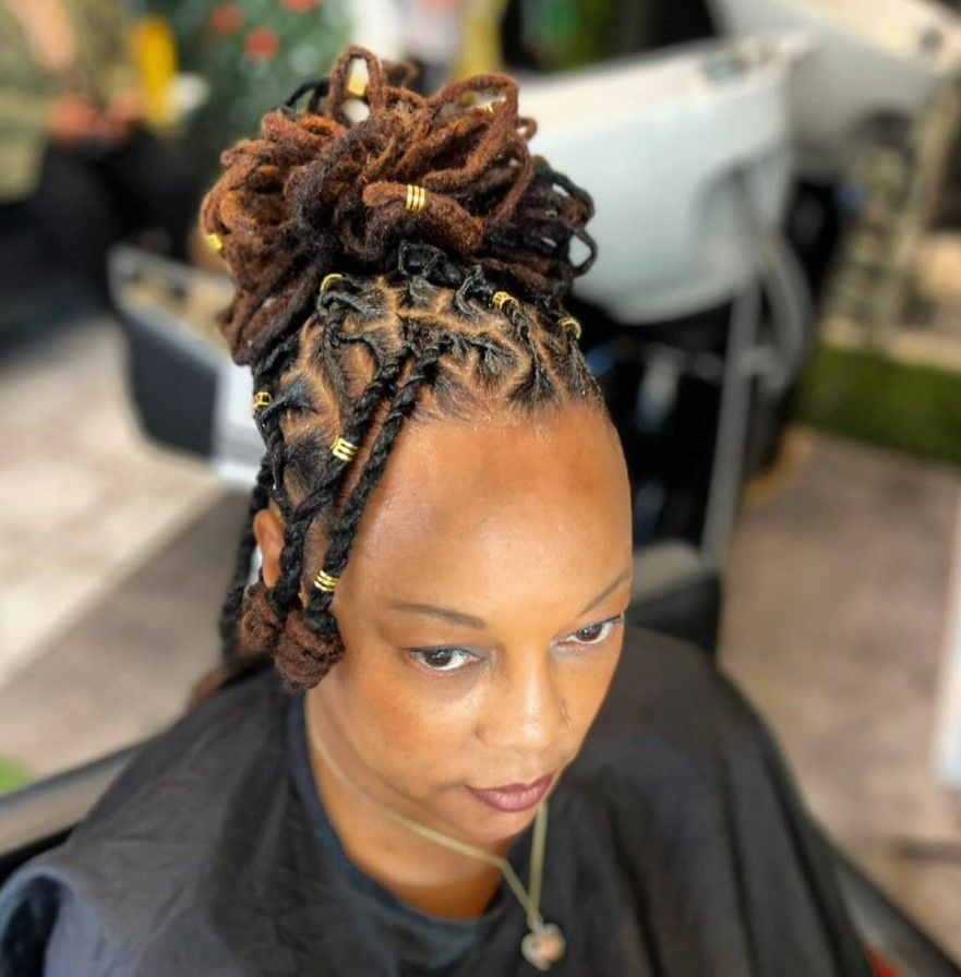 Femme aux fausses dreadlocks brunes coiffées en chignon, quelques mèches s'échappant. Des perles dorées ornent sa chevelure.