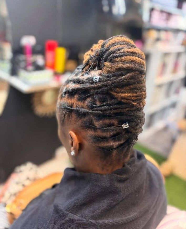 Femme aux dreadlocks brunes et blondes coiffées en un chignon haut orné de perles argentées.