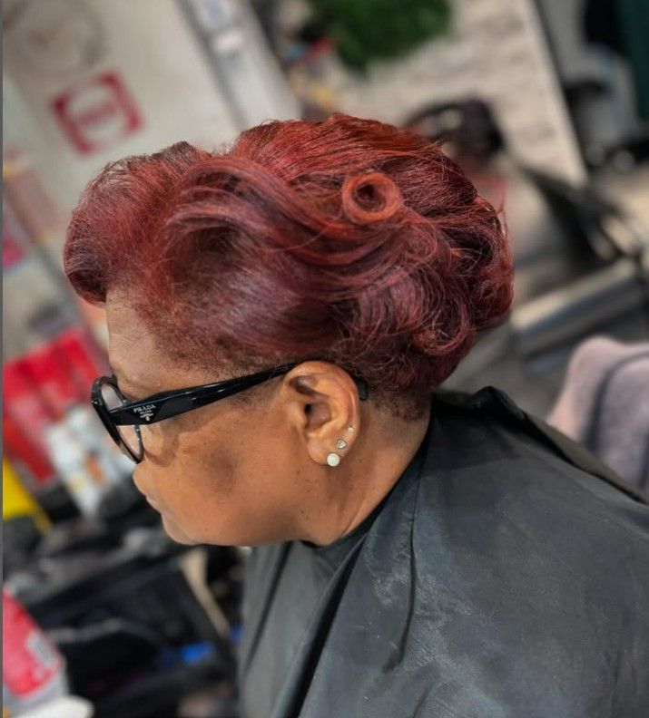 Femme aux cheveux roux foncé coiffés en un chignon sur le côté avec une boucle décorative, portant des lunettes.