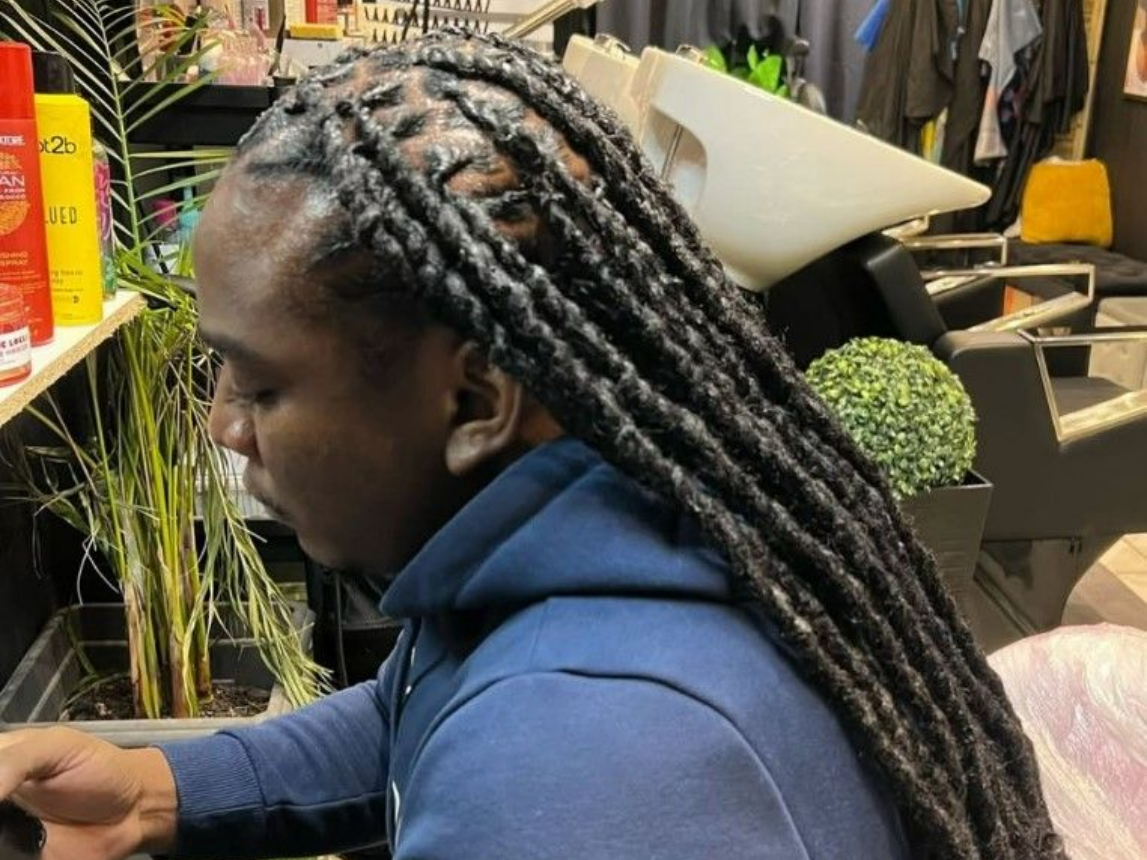Personne aux longues dreadlocks foncées portant un sweat à capuche bleu dans un salon de coiffure.