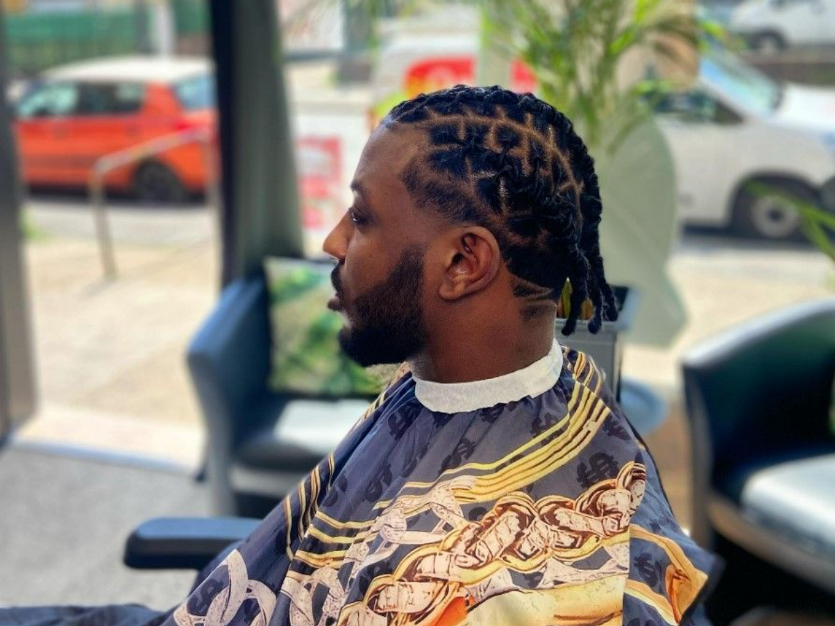 Un homme à la coiffure et à la barbe texturées se trouve dans un salon de coiffure. Il porte une cape à motifs.