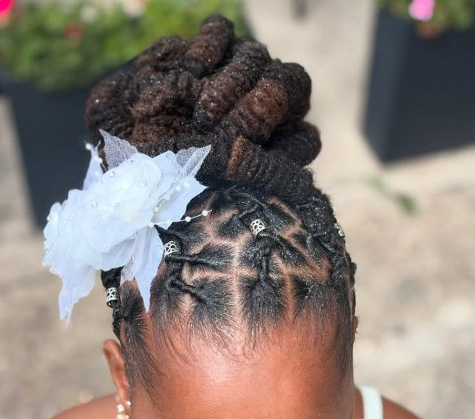 Coiffure tressée ornée d'une fleur. Les tresses sur le haut de la tête sont décorées de perles argentées et d'une fleur blanche.