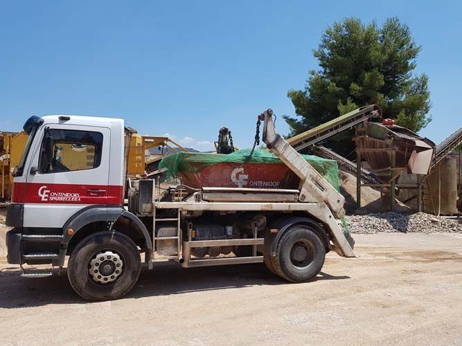 Un camión de obra cargado descarga escombros en una obra bajo un cielo azul despejado