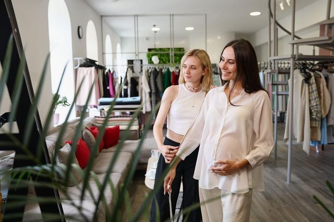 Dos mujeres en una tienda de ropa mirando artículos en los estantes de exhibición y un espejo.