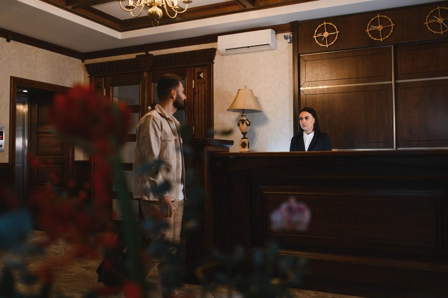 Una persona de pie en la recepción de un hotel con un empleado detrás del mostrador en un vestíbulo con paneles de madera.