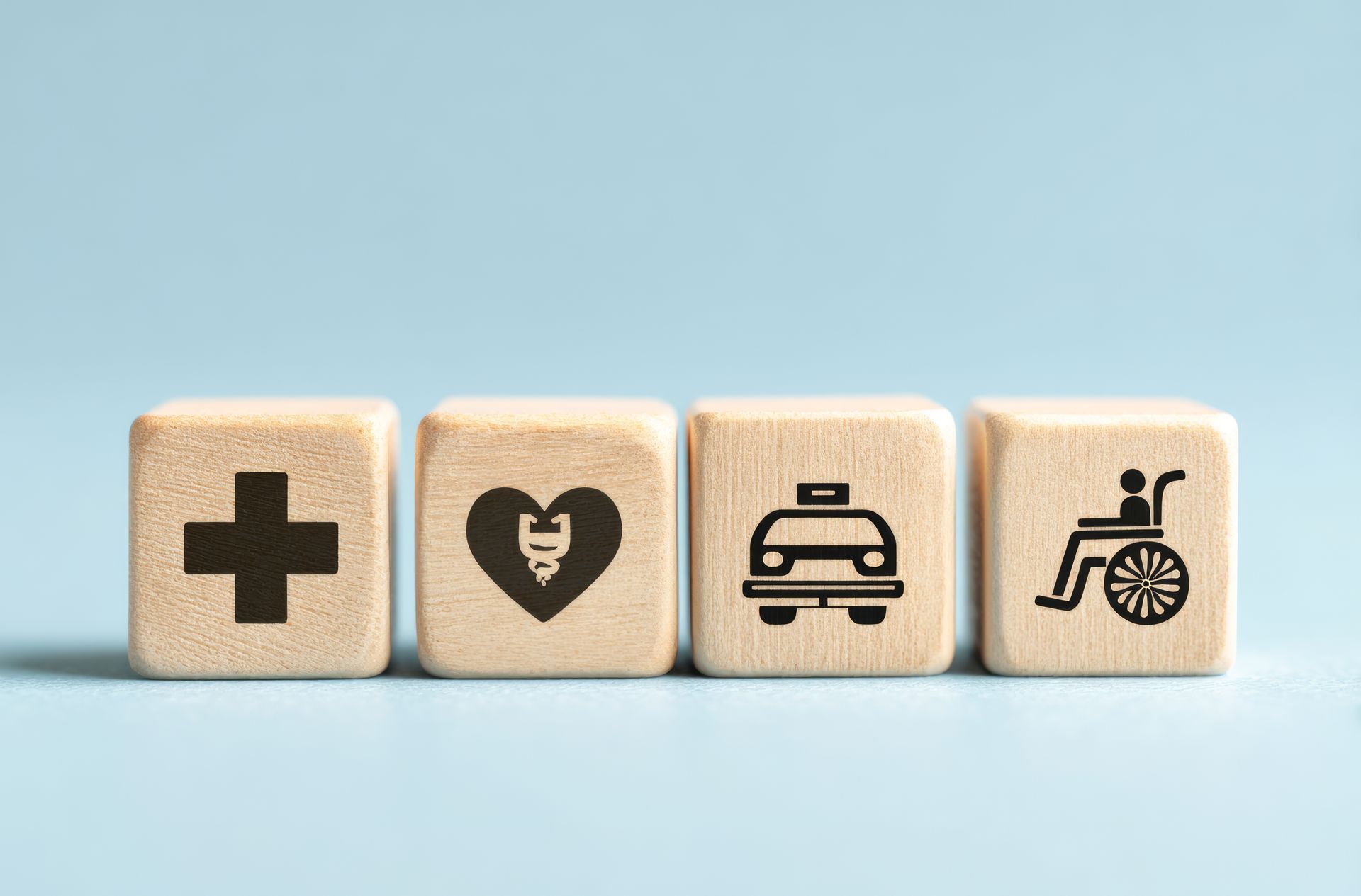 Quatre blocs de bois ornés d'icônes liées à la santé : croix médicale, cœur, voiture et personne en fauteuil roulant.
