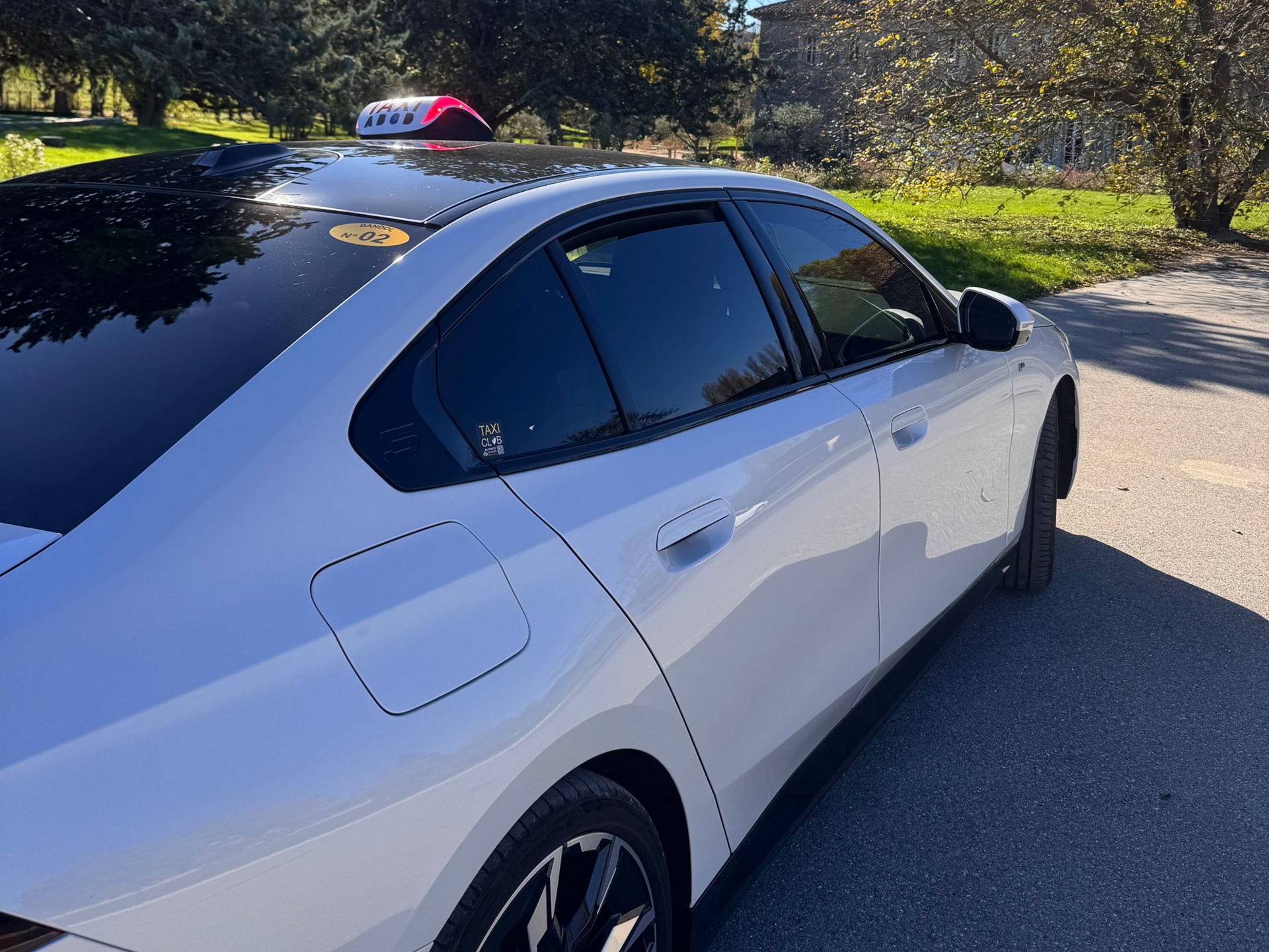 Taxi blanc stationné sur une route goudronnée, en journée. Lumière de toit visible.