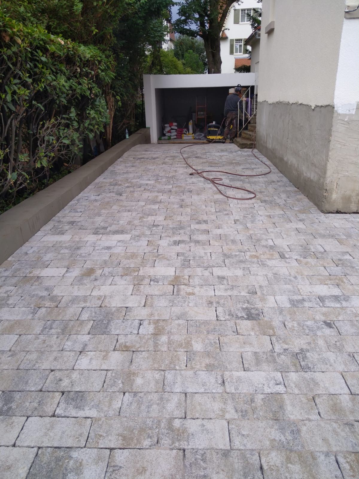 Mit Ziegeln gepflasterte Auffahrt führt zu einer Garageneinfahrt; Bauarbeiten im Gange.