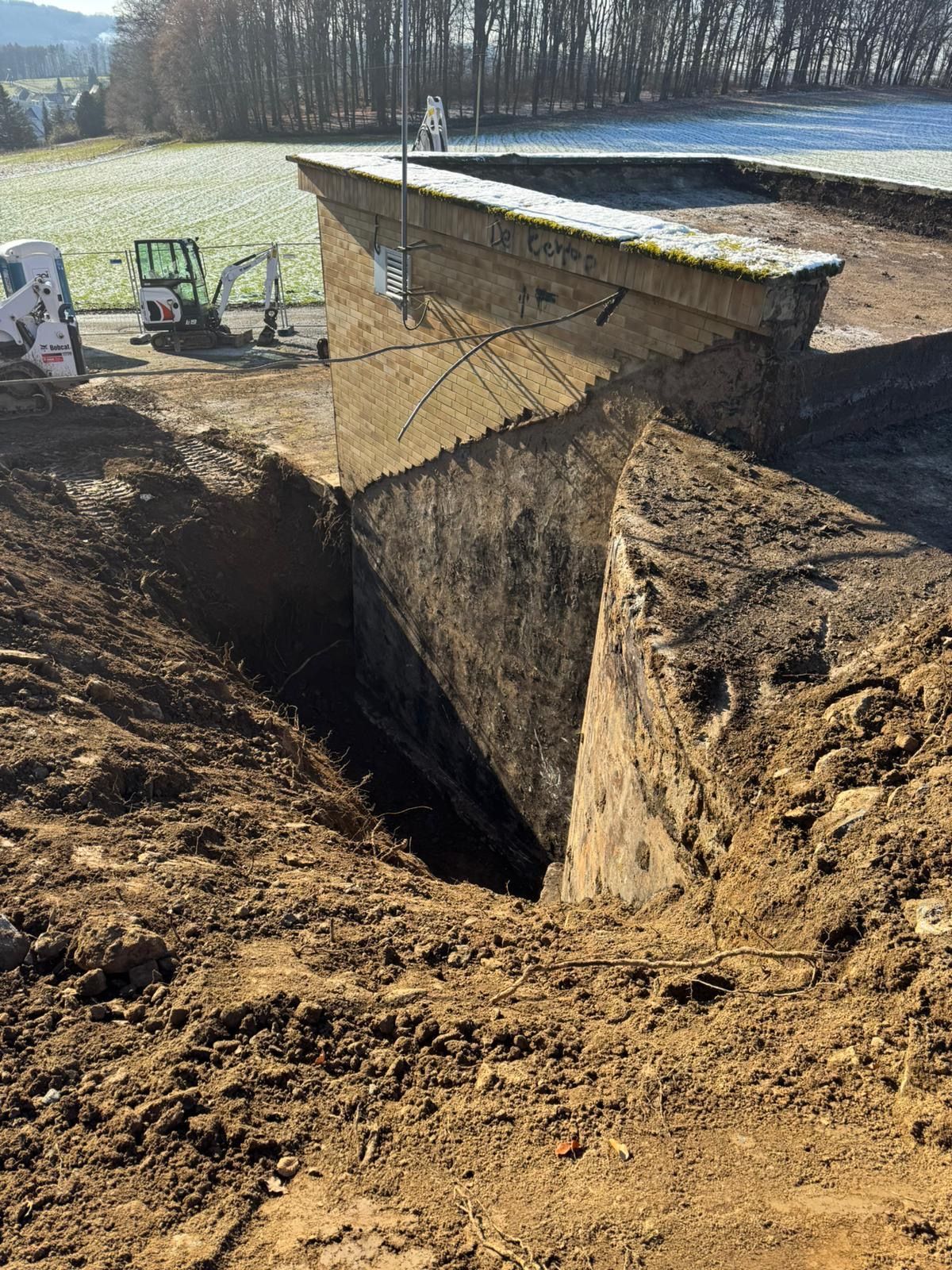 Baustelle: Eine große Betonkonstruktion wird ausgehoben. Erde und Baumaschinen sind sichtbar; sonniger Tag.