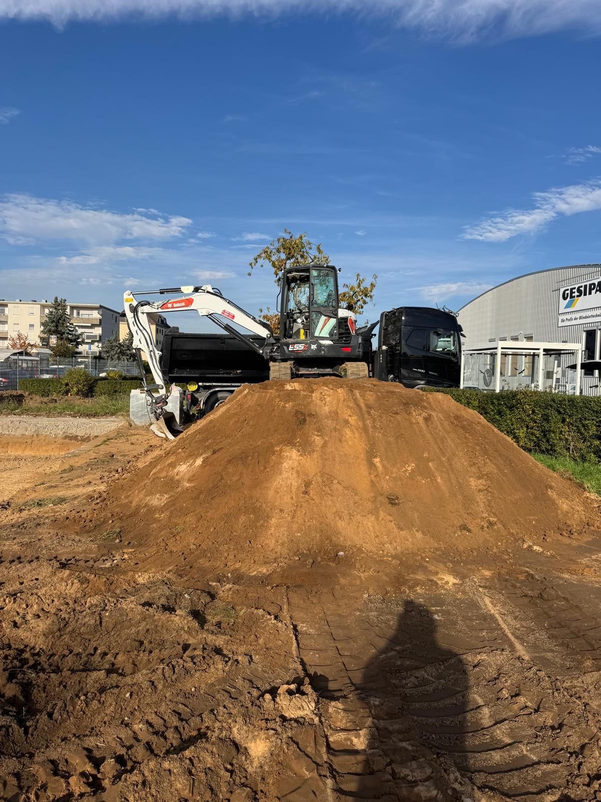 Ein kleiner Bagger steht auf einem Erdhügel auf einer Baustelle unter blauem Himmel.