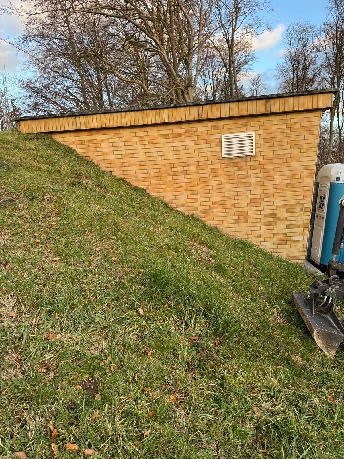 Ein halb in einen grasbewachsenen Hügel eingebettetes Backsteingebäude mit einem Lüftungsgitter.