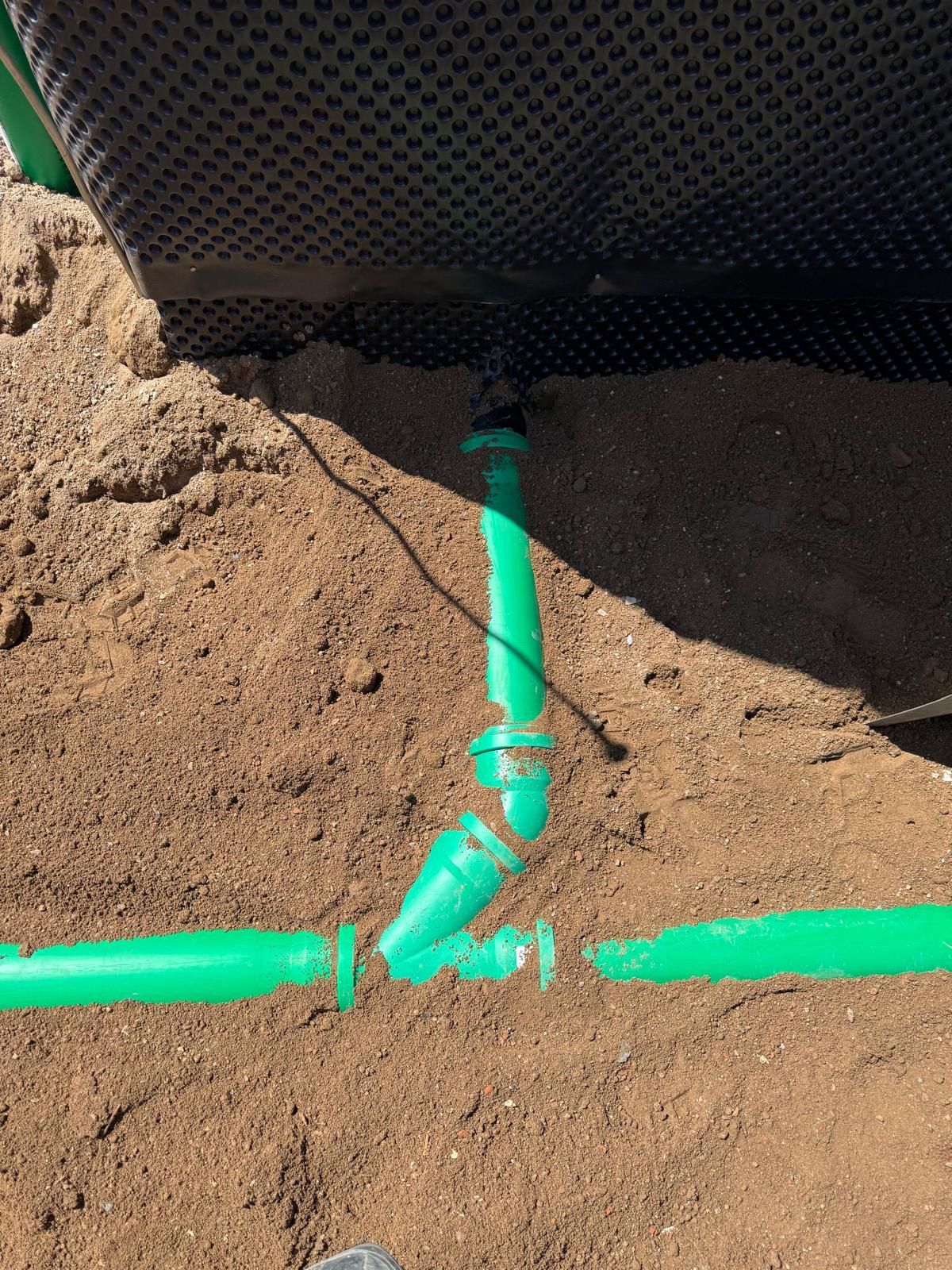 Grüne, im Erdreich unter einer schwarzen Plane verlegte Rohre deuten auf ein Bewässerungs- oder Entwässerungssystem hin.