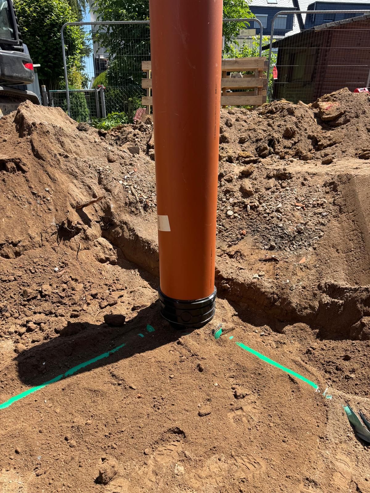 Orangefarbenes Rohr in einer Baugrube; grüne Linien markieren den Boden. Baustellenumgebung.