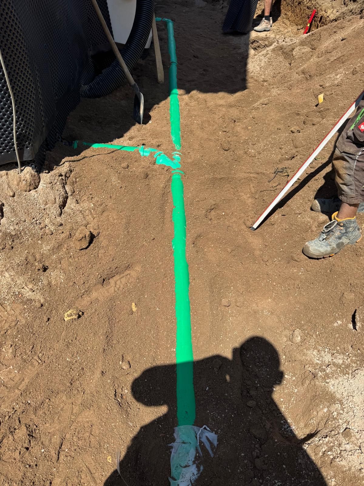 Eine grüne Linie ist auf den Boden gesprüht und markiert einen Weg. Baustelle; der Schatten einer Person mit Stock ist sichtbar.