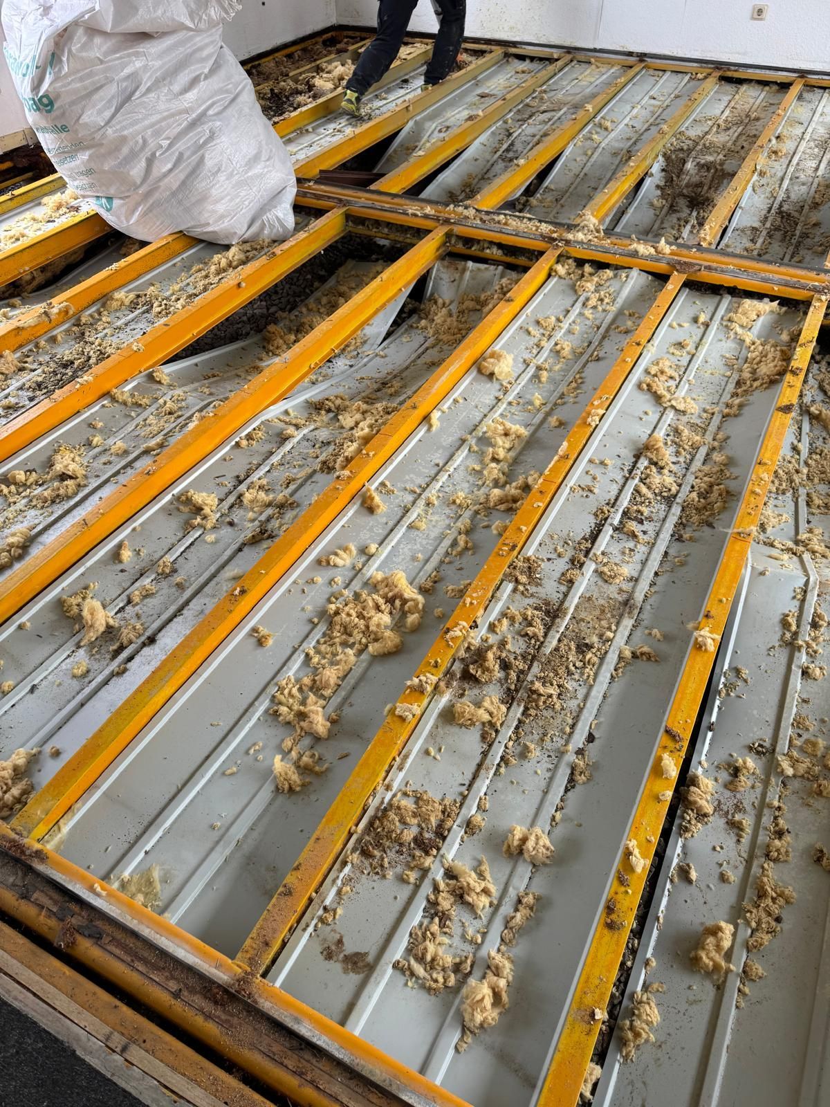 Eine Person schüttet Dämmmaterial in eine gelb umrahmte Bodenkonstruktion, Ansicht von oben.