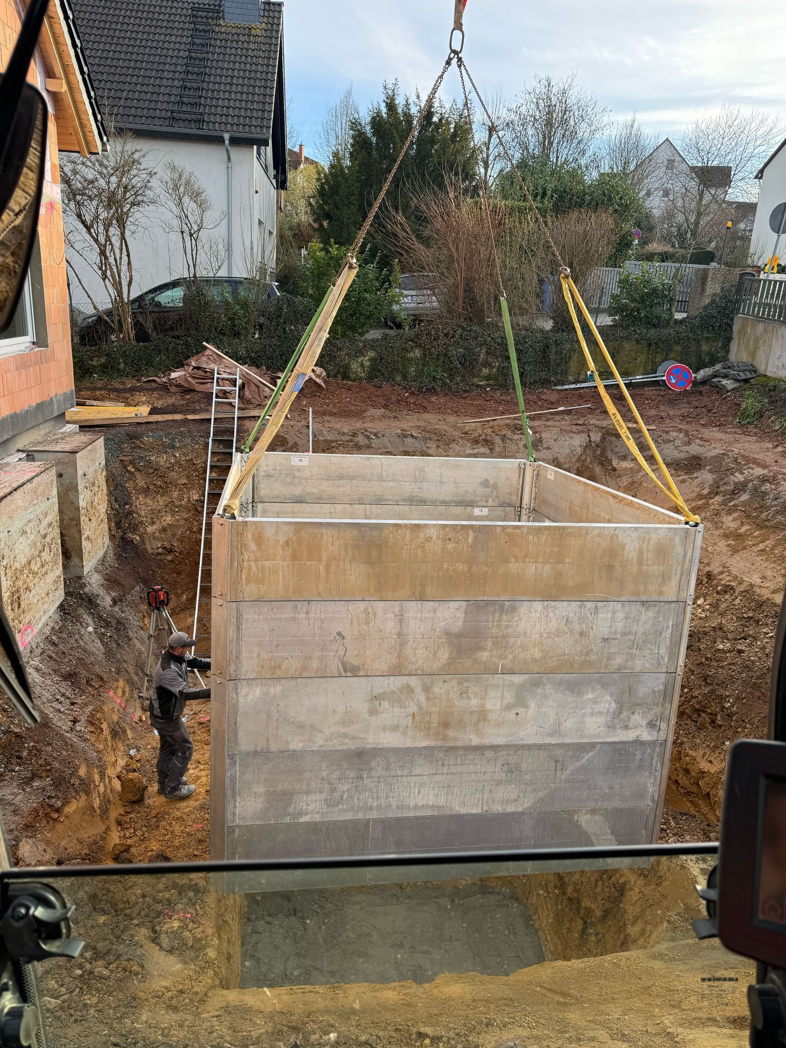 Auf einer Baustelle wird ein großer Betonkasten in eine quadratische Baugrube gehoben.