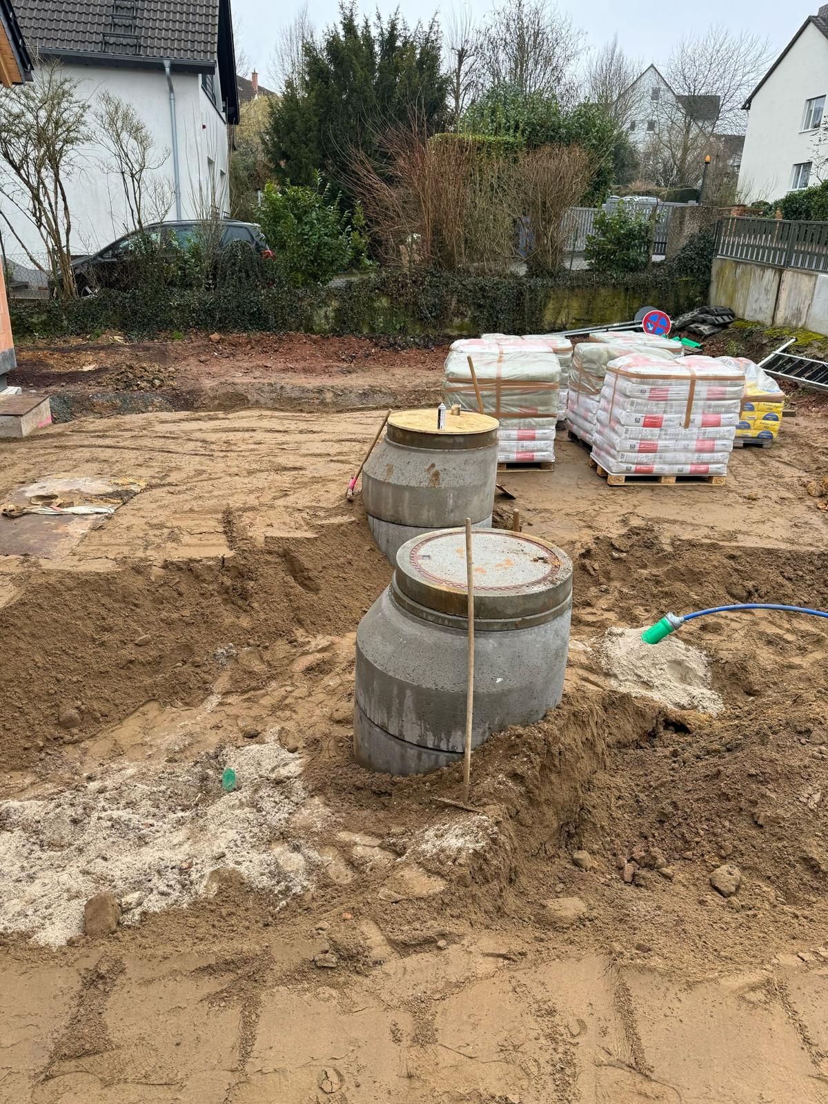 Baustelle mit Betonzylindern, Sand und Ziegelstapeln.