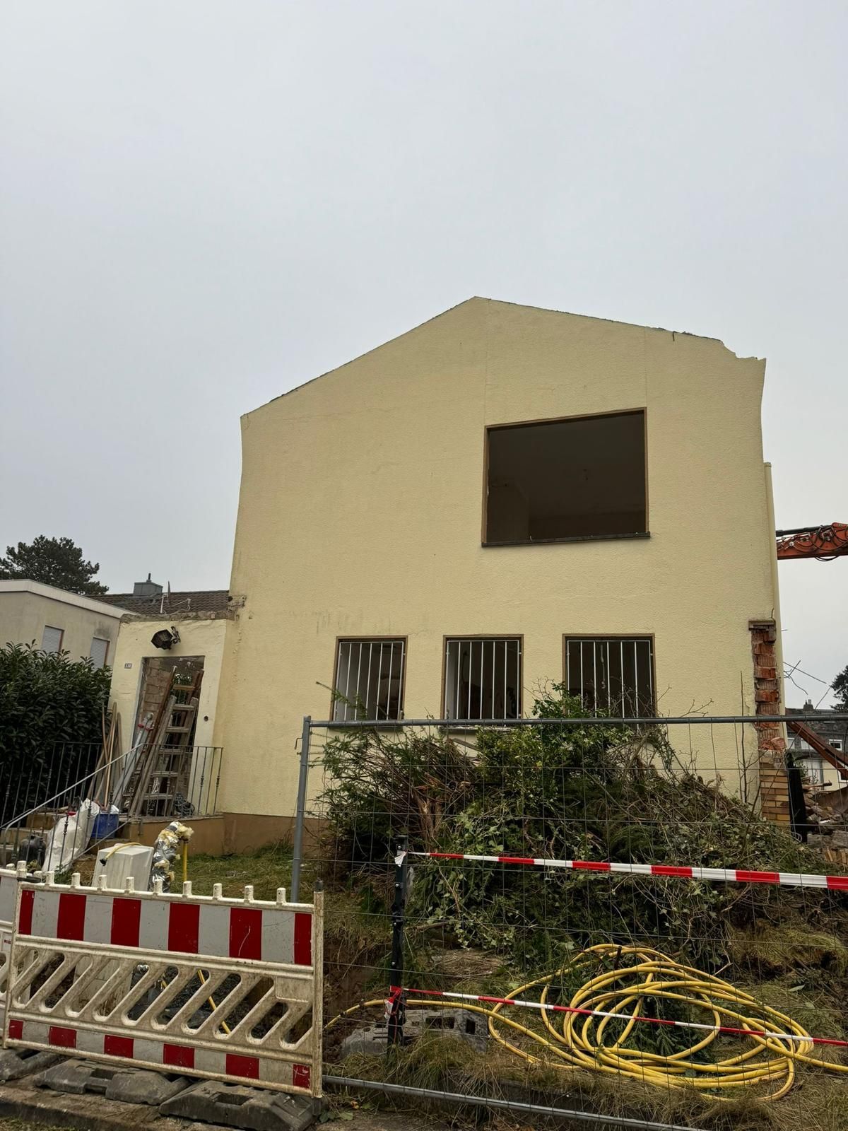 Ein teilweise abgerissenes Haus hinter einem Bauzaun, der Himmel ist bedeckt.