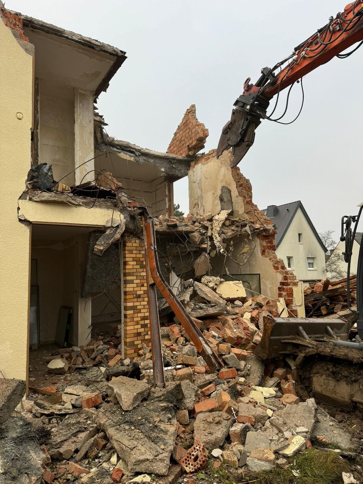 Abriss eines Backsteingebäudes durch einen Bagger an einem bewölkten Tag.