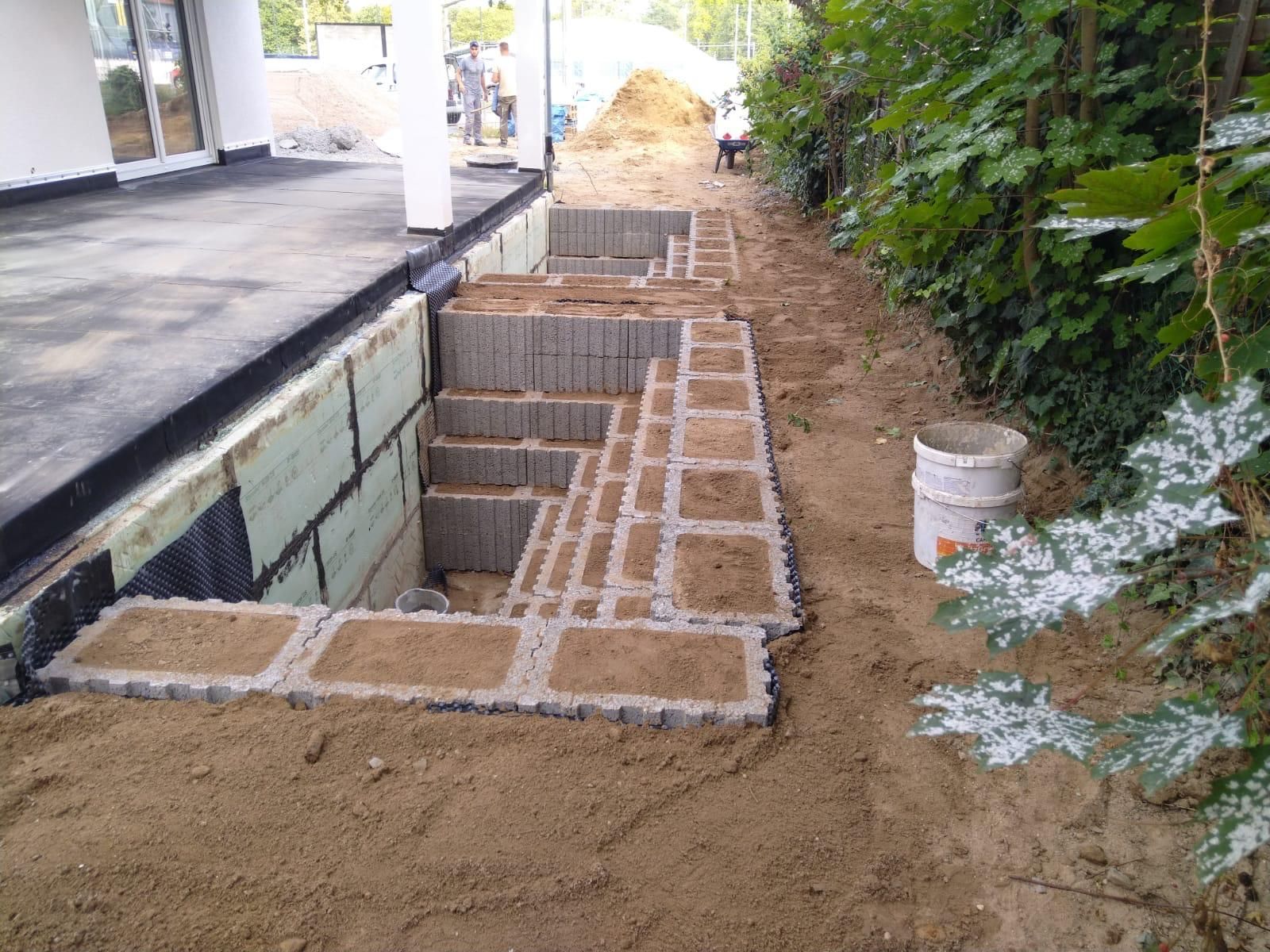 Errichtung einer Außentreppe aus grauen Blöcken und Sand neben einem Gebäude.