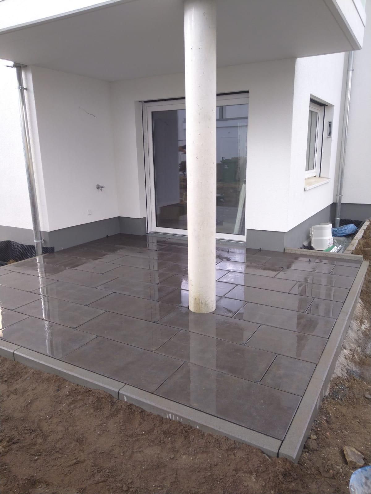 Terrasse mit dunkelgrauen Fliesen, weißer Säule und moderner Hausfassade.