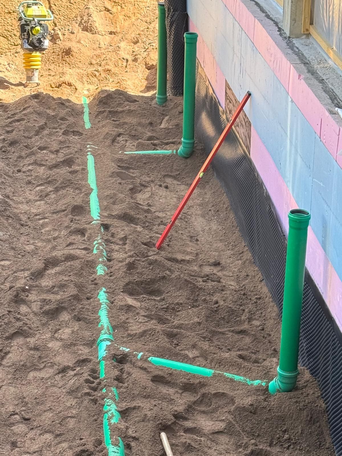 Grüne Rohre wurden entlang einer Fundamentwand auf einer Baustelle verlegt.