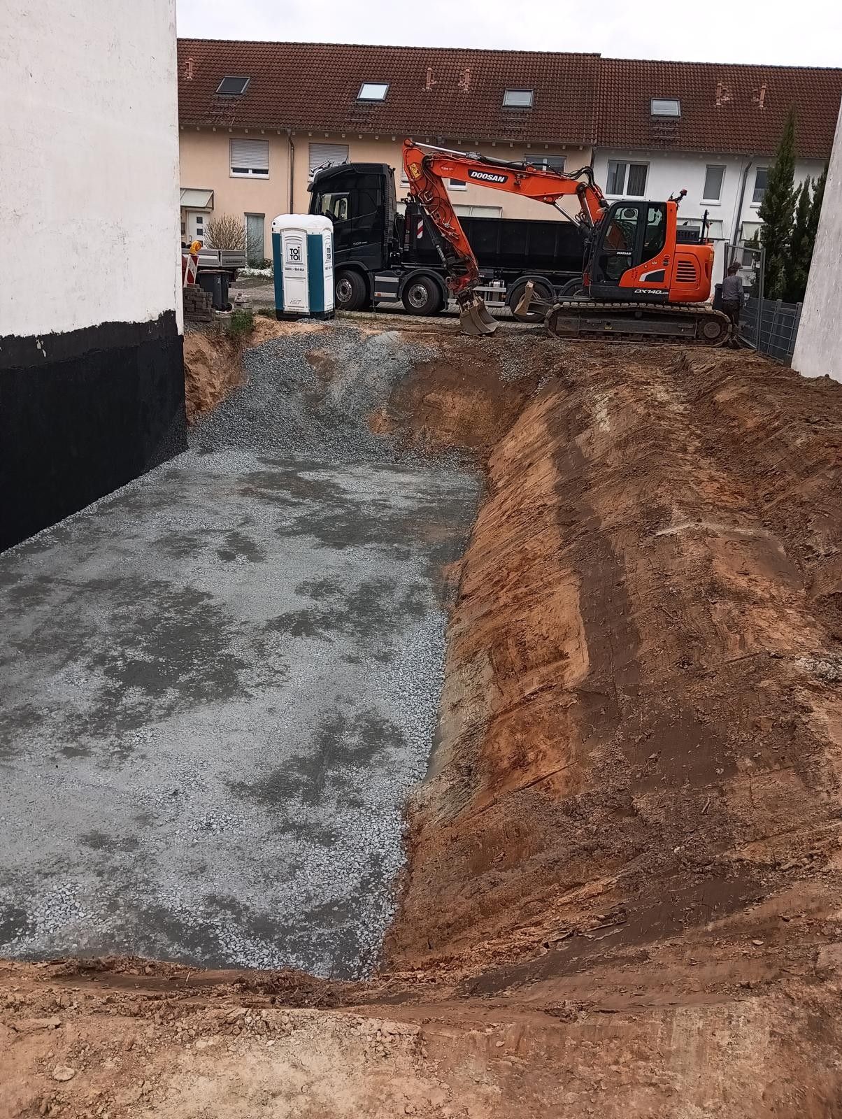 Baugrube mit Schotterbett, Erdwänden und Baumaschinen. Inklusive LKW und Bagger.