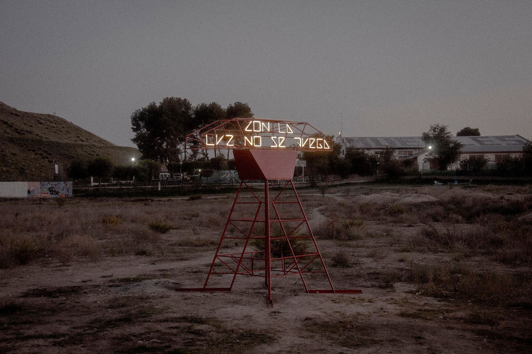 Estructura de metal rojo en un campo, letrero iluminado que dice 