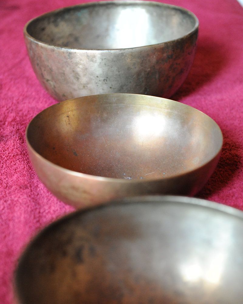 Drei Klangschalen aus Metall in verschiedenen Größen, in einer Reihe aufgestellt.