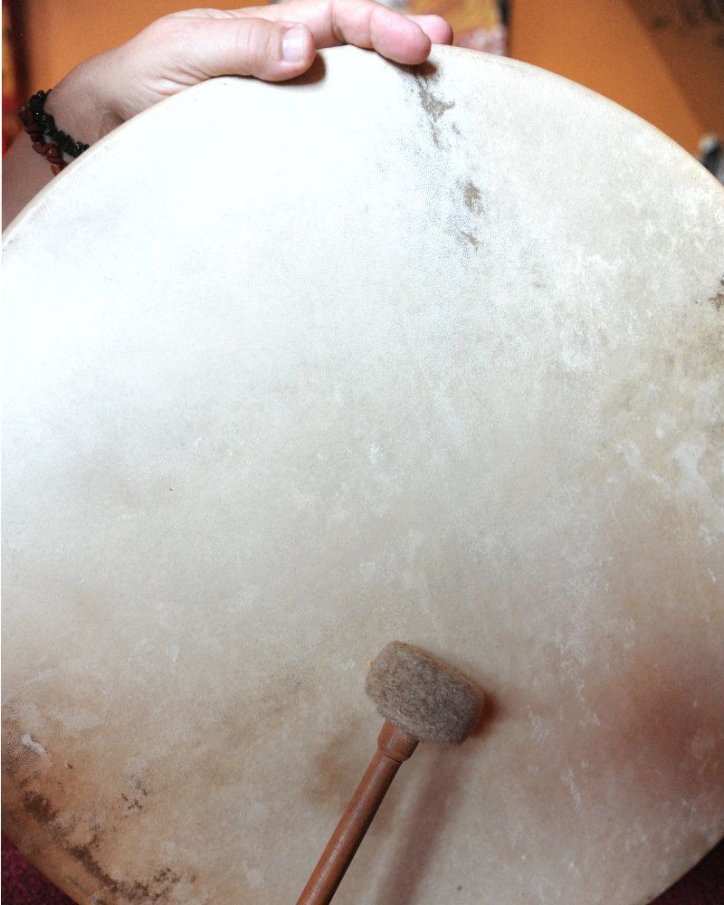 Eine Person hält in ihrer Hand eine große, runde Trommel. Auf der Oberfläche der Trommel liegt ein Schlägel.