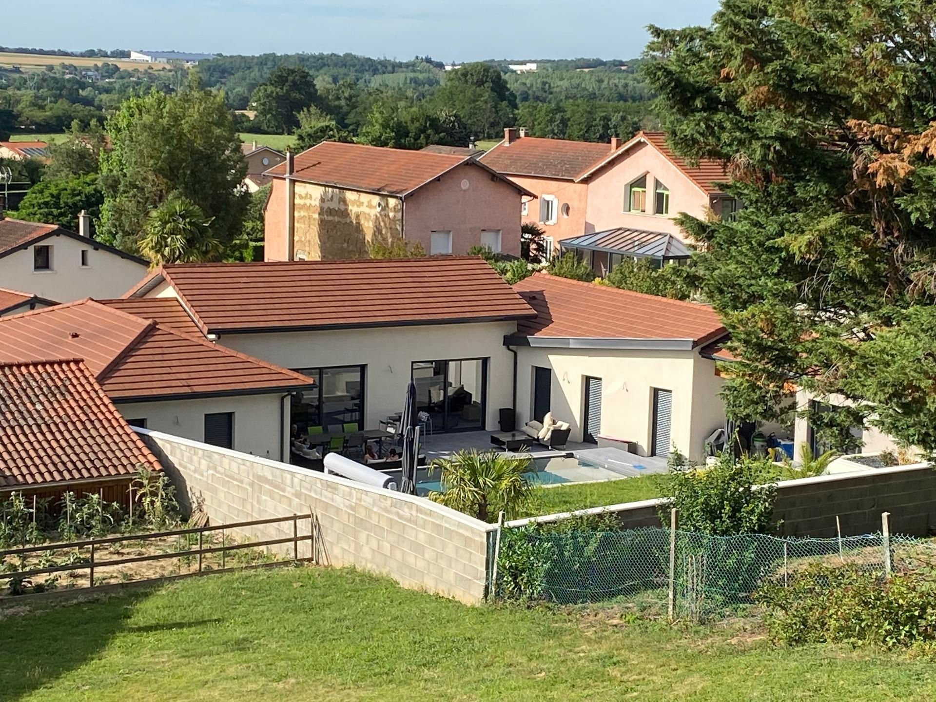 Scène résidentielle avec des maisons et une piscine dans une cour, des arbres et de l'herbe verte.