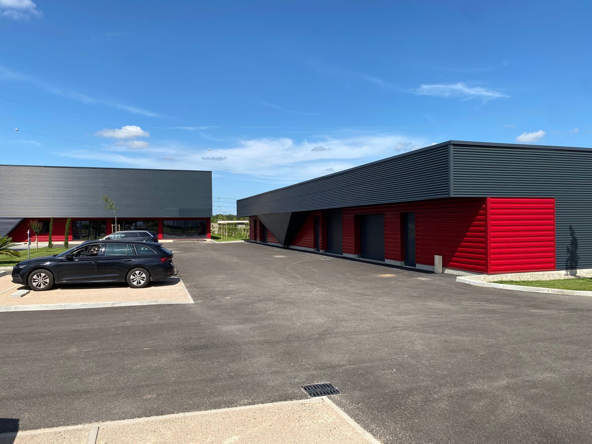 Bâtiment commercial moderne avec revêtement en tôle ondulée noire et accent rouge, sous un ciel bleu.